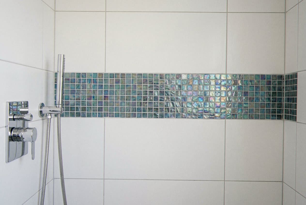 Iridescent mosaic accent band across a white tile shower